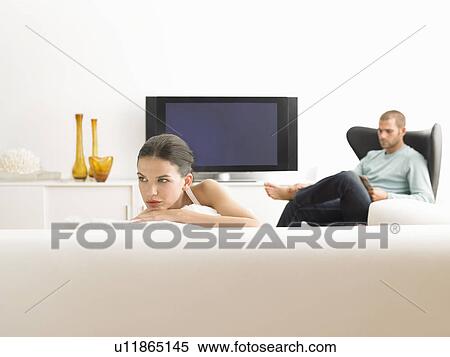 Stock Photography - Woman on sofa and man in armchair in modern living room. Fotosearch