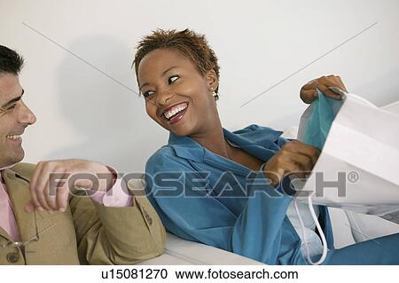 Stock Image - Woman on sofa Showing Man Purchases from Shopping Bag. Fotosearch
