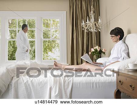 Woman reading newspaper in bed, husband looking through window View Large Photo Image Stock Photo - Woman reading newspaper in bed, husband looking through window. Fotosearch
