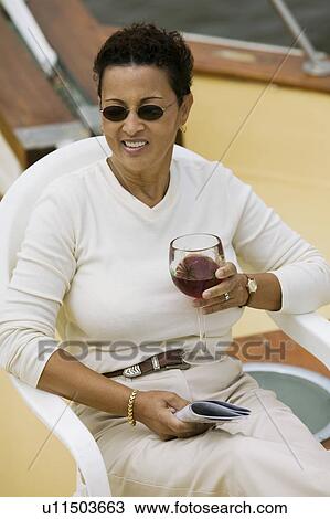 Stock Image - Woman relaxing on yacht, holding glass of red wine. Fotosearch