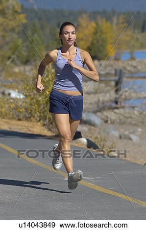 Stock Photo - Woman running along road by woodland. Fotosearch