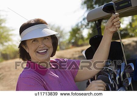 Stock Photo - Woman selecting golf club from golf cart, smiling, (portrait). Fotosearch