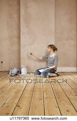 Stock Image - Woman sitting on floor of unrenovated room, looking at colour paint swatches. Fotosearch