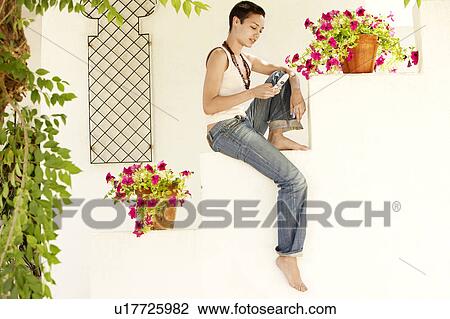 Woman Sitting on wall in garden, using mobile phone. View Large Photo Image Stock Image - Woman Sitting on wall in garden, using mobile phone.. Fotosearch