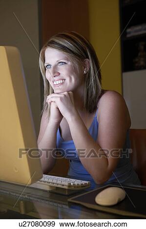 Stock Photo - Woman smiling sitting in front of computer screen. Fotosearch
