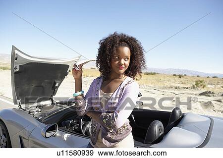 Stock Photo - Woman standing by broken down sports car at side of desert road. Fotosearch