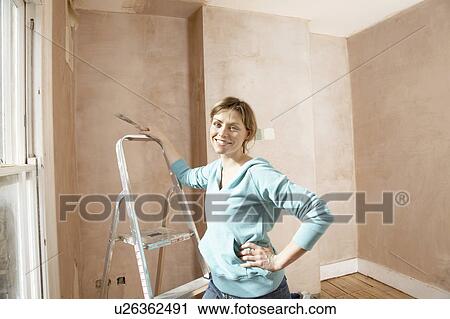 Stock Image - Woman standing by step ladder with scraping tool in hand. Fotosearch