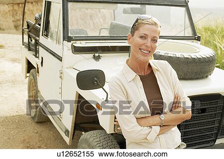 Stock Photography - Woman standing in front of four wheel drive car in desert, portrait. Fotosearch