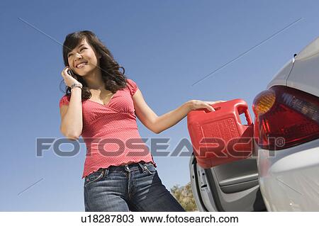 Stock Image - Woman stands with mobile phone while refuelling car from canister. Fotosearch