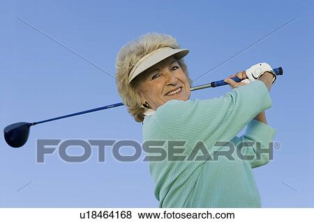 Woman swinging golf club, (portrait), (low angle view) View Large Photo Image Stock Photo - Woman swinging golf club, (portrait), (low angle view). Fotosearch