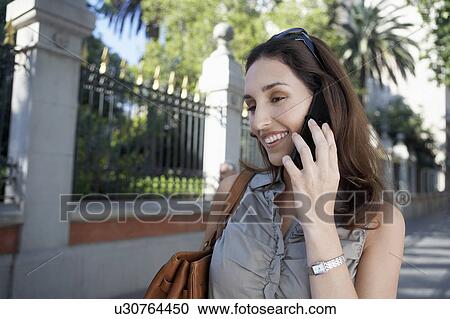 Stock Image - Woman using cell phone on sidewalk. Fotosearch