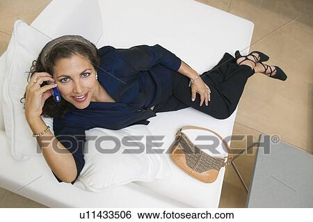 Stock Photograph - Woman Using Cell Phone on Sofa, portrait, high angle view. Fotosearch