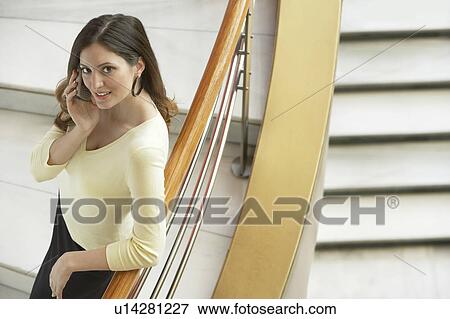 Stock Photo - Woman using mobile phone, leaning on railing of staircase, elevated view.. Fotosearch