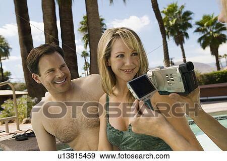 Stock Photo - Woman Video Taping Couple by pool.. Fotosearch