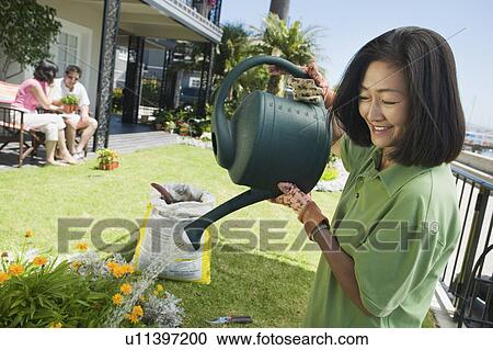 Stock Image - Woman watering plants in garden. Fotosearch