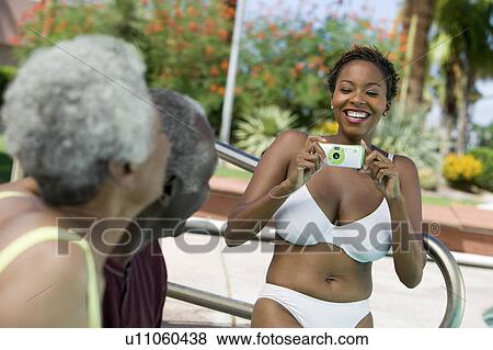 Stock Photo - Woman wearing bikini photographing senior couple outdoors.. Fotosearch