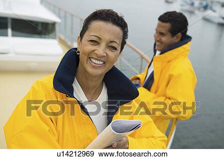 Stock Photo - Woman wearing yellow anorak on yacht, husband in background, (portrait). Fotosearch