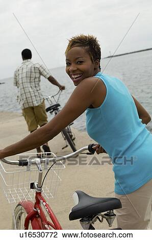 Stock Image - Woman with bicycle at beach, (portrait). Fotosearch