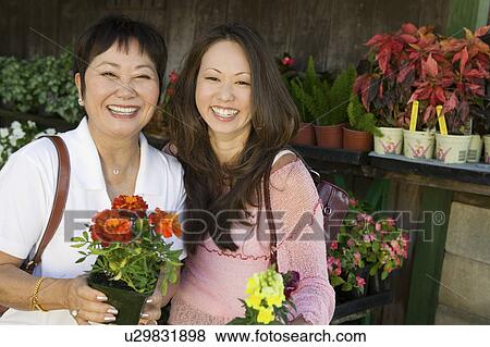 Woman with mother holding flowers in plant nursery, portrait View Large Photo Image Stock Photo - Woman with mother holding flowers in plant nursery, portrait. Fotosearch