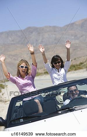 Stock Photo - Women in convertible with hands raised. Fotosearch