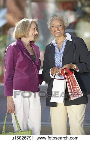 Stock Image - Women standing side by side outside holding shopping bags on Shopping Trip. Fotosearch