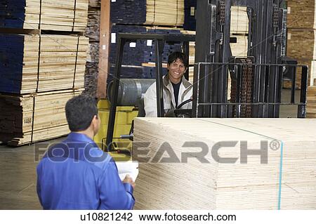 Stock Image - Workers with forklift carrying wood in warehouse. Fotosearch