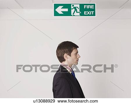 Stock Photo - Young businessman standing under exit sign. Fotosearch