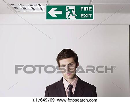 Stock Photo - Young businessman standing under exit sign. Fotosearch