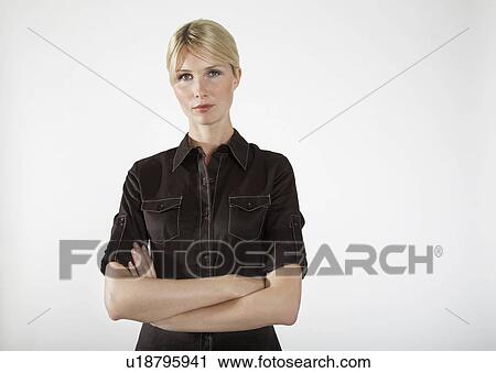 Stock Image - Young businesswoman with arms crossed, on white background, portrait. Fotosearch