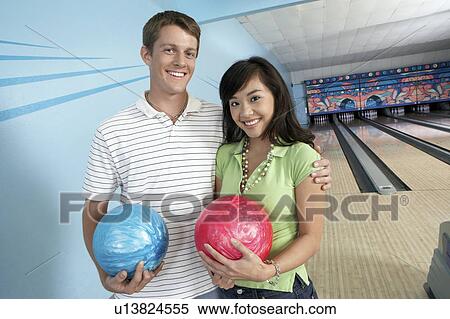 Stock Photography - Young couple at bowling alley holding balls, portrait. Fotosearch