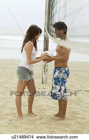 Picture - Young couple Both Holding Volleyball under Net on Beach, side view. Fotosearch