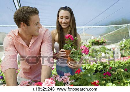 Stock Image - Young couple choosing potted flowers in garden center. Fotosearch