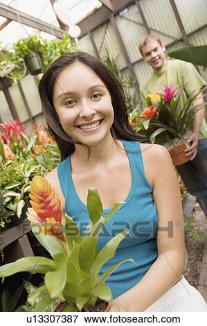Young couple holding carrying potted plant in greenhouse, (portrait) View Large Photo Image Stock Photo - Young couple holding carrying potted plant in greenhouse, (portrait). Fotosearch