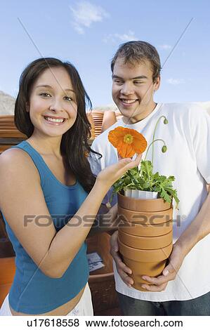 Stock Photo - Young couple holding flower pots in outdoors garden centre, (portrait). Fotosearch
