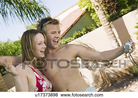 Young couple in swimwear photographing selves in back yard View Large Photo Image Stock Photo - Young couple in swimwear photographing selves in back yard. Fotosearch