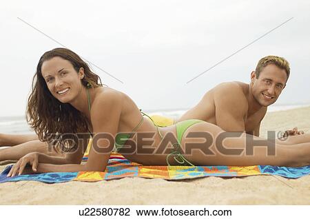 Young couple lying down on beach on towel, portrait, side view View Large Photo Image Stock Image - Young couple lying down on beach on towel, portrait, side view. Fotosearch