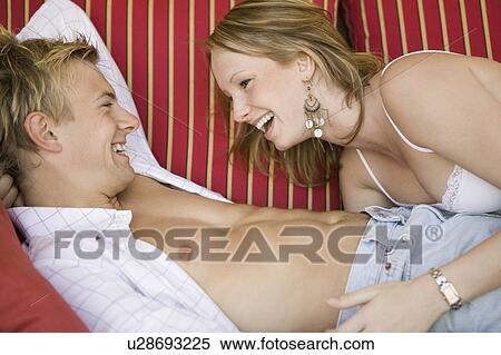 Stock Photography - Young couple lying on sofa together, side view. Fotosearch