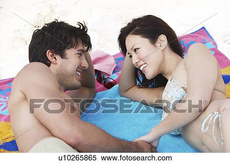 Stock Photography - Young couple lying on towel at beach. Fotosearch