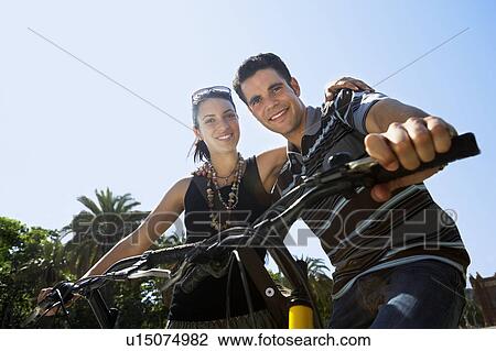 Stock Image - Young couple on bikes, portrait, low angle view. Fotosearch