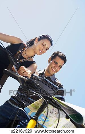 Young couple on bikes reading map, low angle view View Large Photo Image Stock Photo - Young couple on bikes reading map, low angle view. Fotosearch