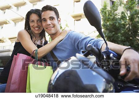 Young couple on motor scooter with shopping bags, portrait View Large Photo Image Stock Photo - Young couple on motor scooter with shopping bags, portrait. Fotosearch