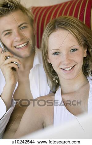 Young couple on sofa, man on cell phone, portrait View Large Photo Image Picture - Young couple on sofa, man on cell phone, portrait. Fotosearch
