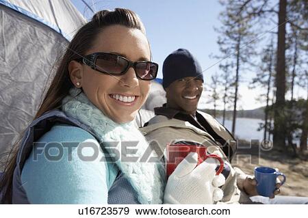Stock Photo - Young Couple sitting at campsite, drinking from mugs.. Fotosearch