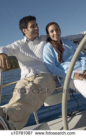 Stock Photo - Young couple sitting at steering wheel on sailboat. Fotosearch