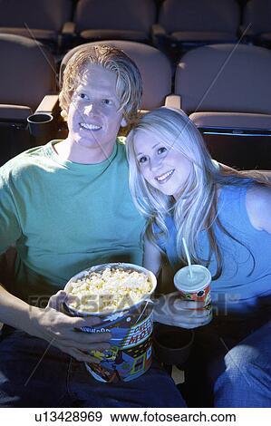 Stock Photo - Young Couple sitting close, lying on shoulder Watching Movie Together in theatre. Fotosearch