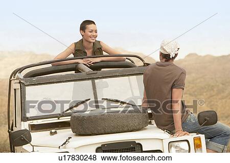 Stock Photo - Young couple sitting in stationary four wheel drive vehicle in desert. Fotosearch