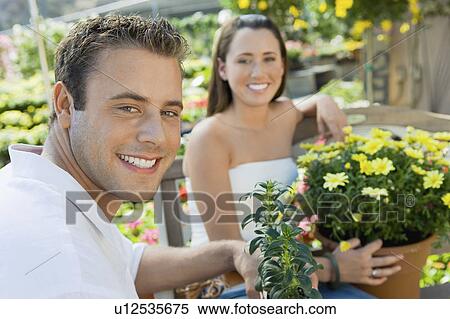 Stock Photography - Young couple sitting on bench in garden centre, (portrait). Fotosearch