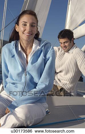 Stock Photograph - Young couple sitting on sailboat, focus on woman, (portrait). Fotosearch