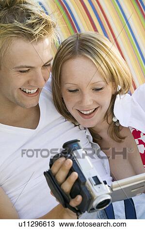 Young couple sitting on sofa looking at video camera screen, close up View Large Photo Image Stock Image - Young couple sitting on sofa looking at video camera screen, close up. Fotosearch