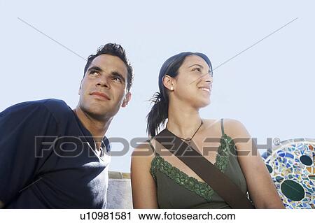Stock Image - Young couple sitting on stone bench, portrait. Fotosearch